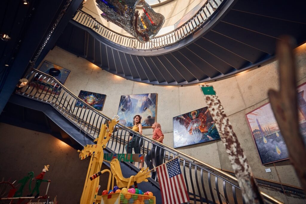 Two people walking up a staircase with sculpture hanging at the center