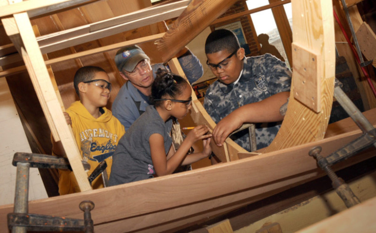 Children making a wooden boat with an instructor.