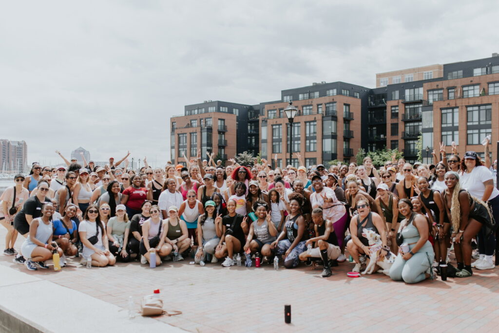 A large group of women smile on the boardwalk in FEll's Point