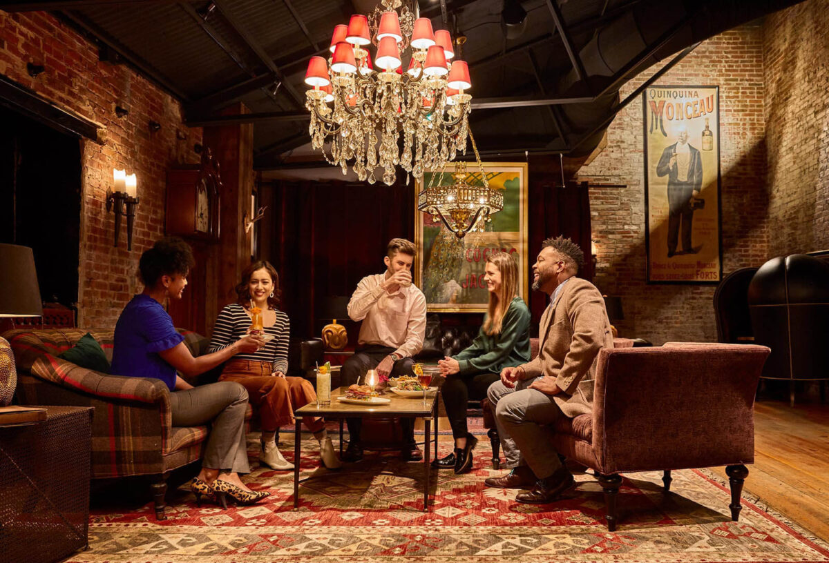 Five customers enjoy drinks on couches and chairs underneath a chandelier at the Elk Room in Baltimore.