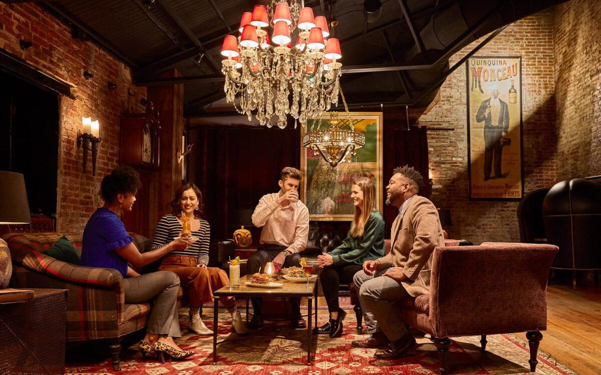 Five customers enjoy drinks on couches and chairs underneath a chandelier at the Elk Room in Baltimore.