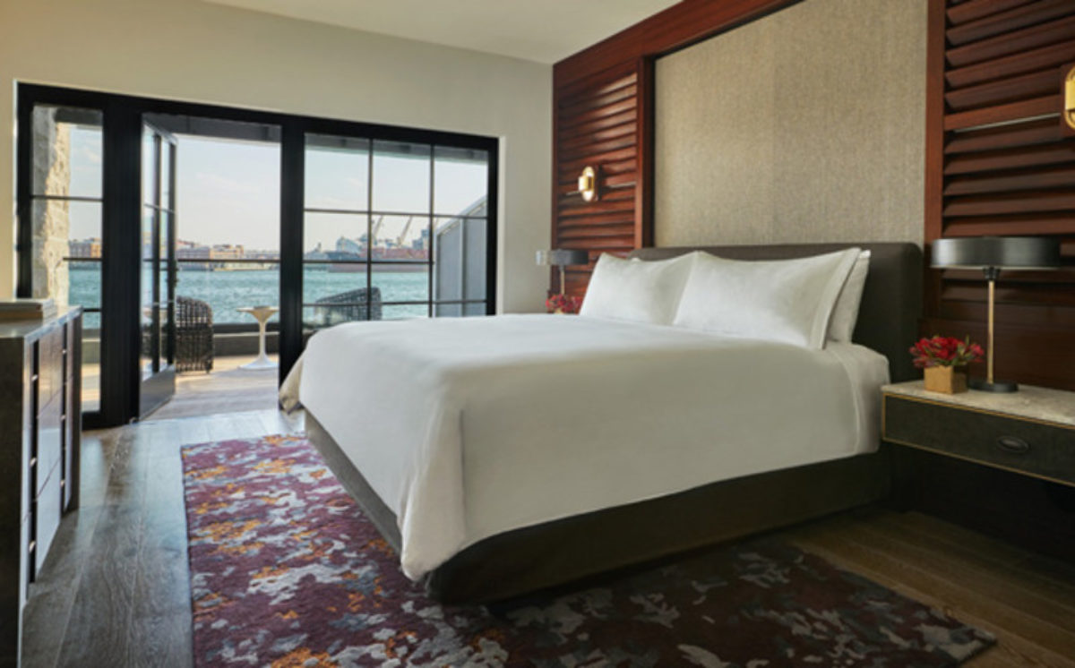Hotel room with a large bed and a view of the harbor in the window.