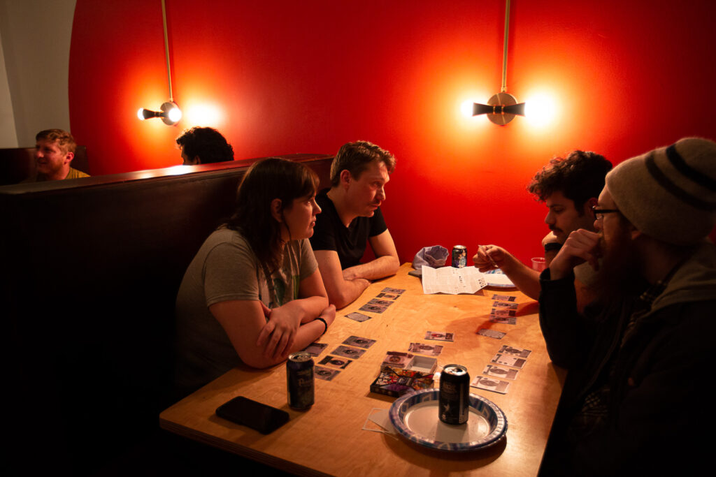 Friends play a board game in a dimly-lit bar booth