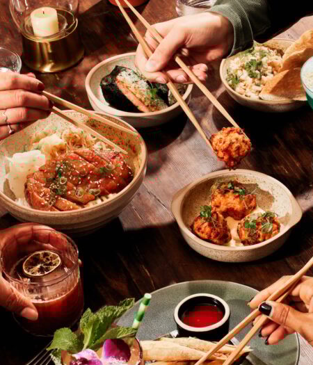 Hands holding chopsticks hover over small plates