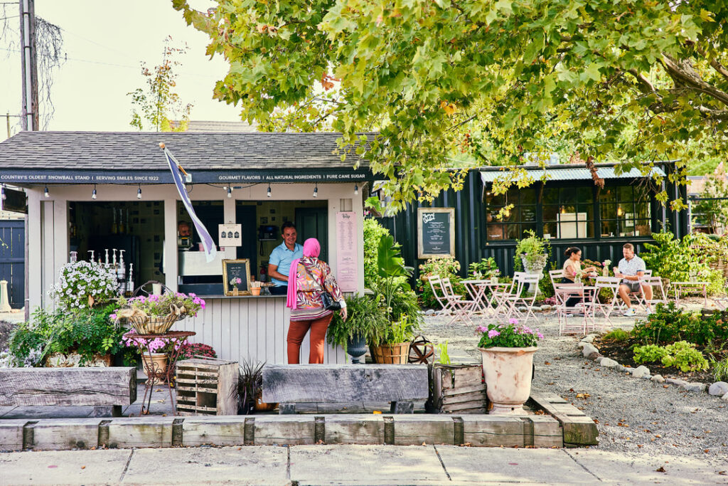 A woman in a pink hijab orders from an outdoor snowball stand