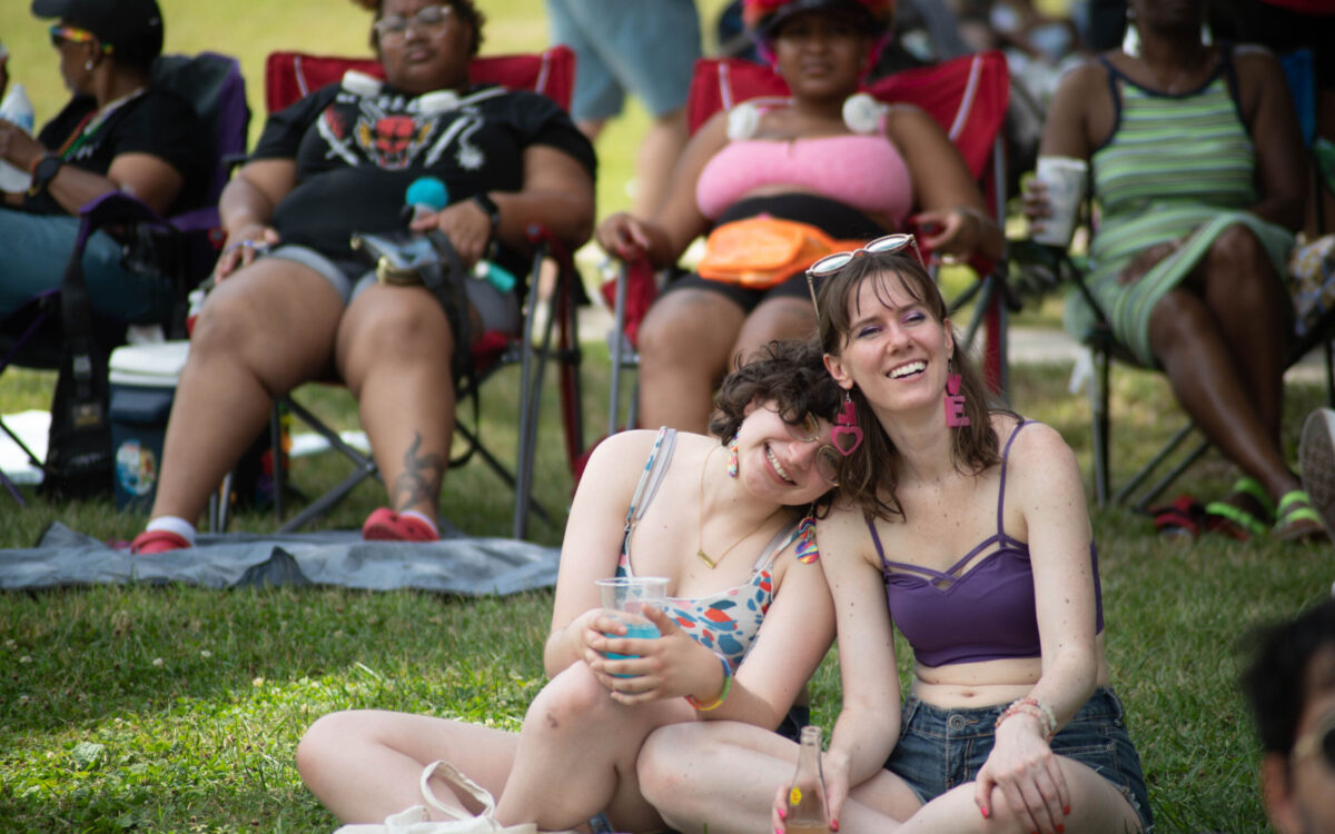 The white women lean into each other while sitting on a lawn