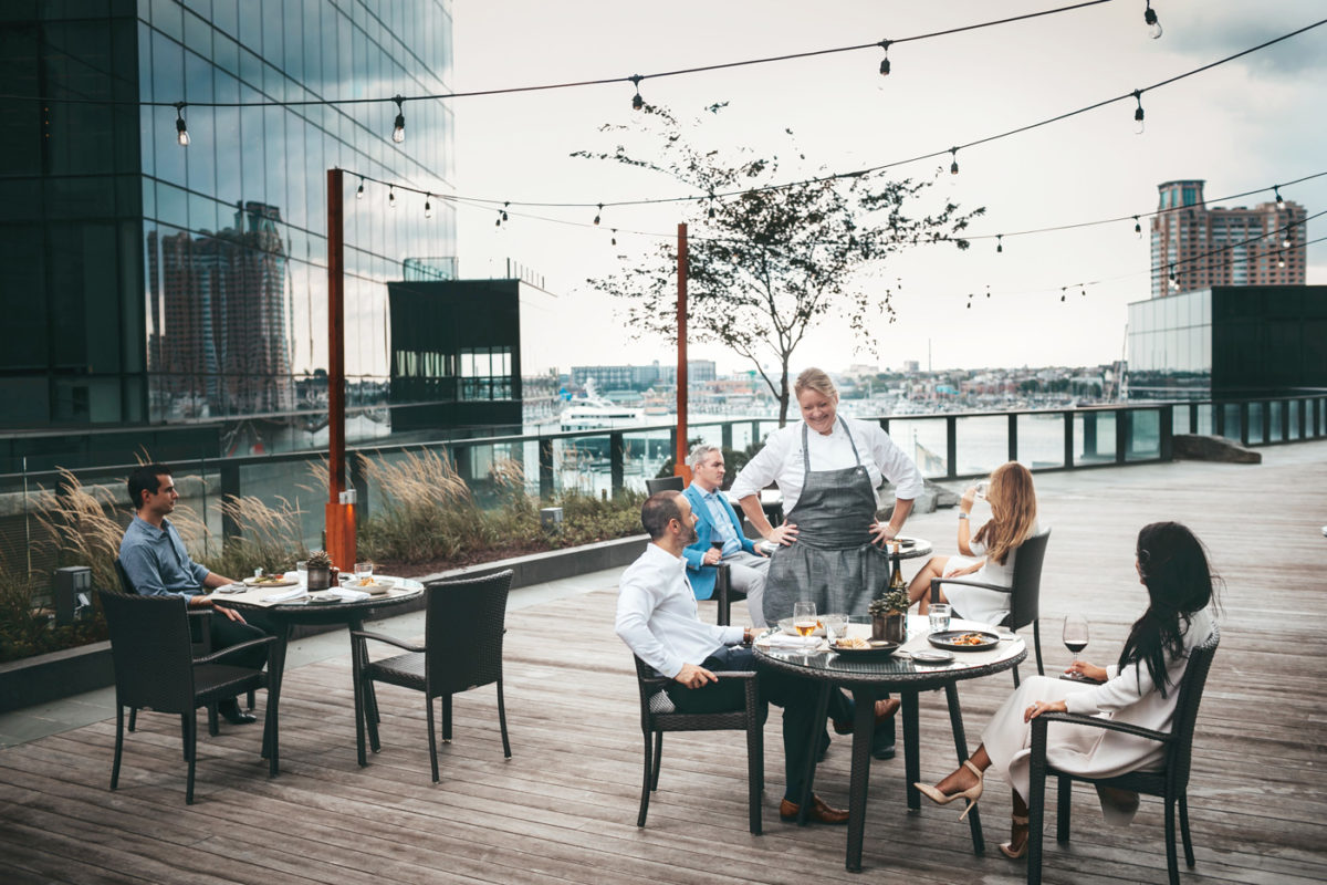 Diners sitting at tables on the boardwalk by the water on a cloudy day.